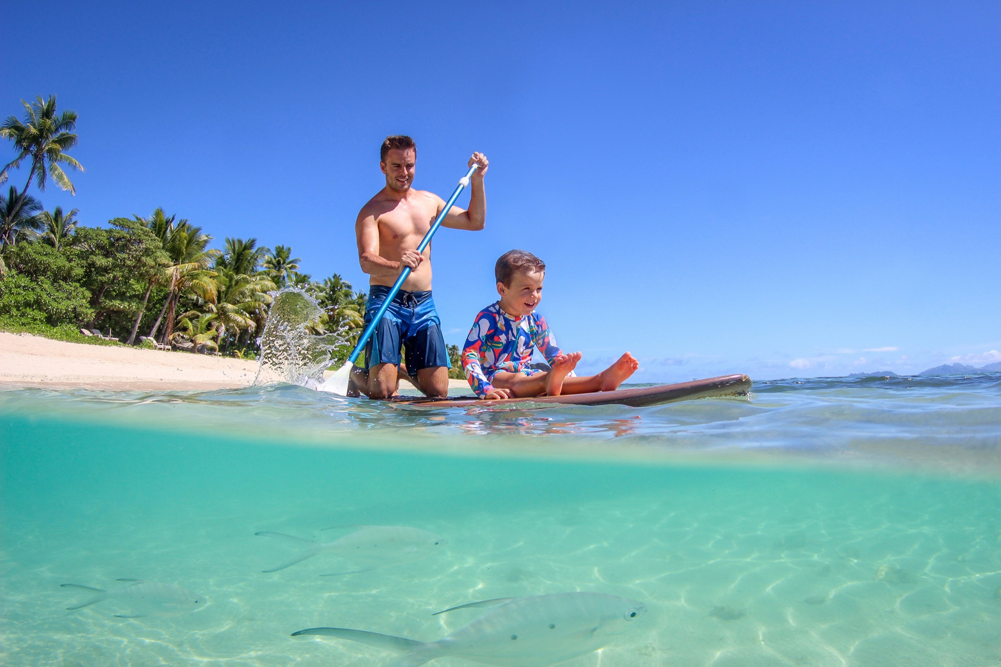 Father and son paddleboarding in clear Fijian water