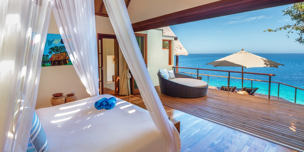 Canopy bed in a bure opening onto a deck above the ocean