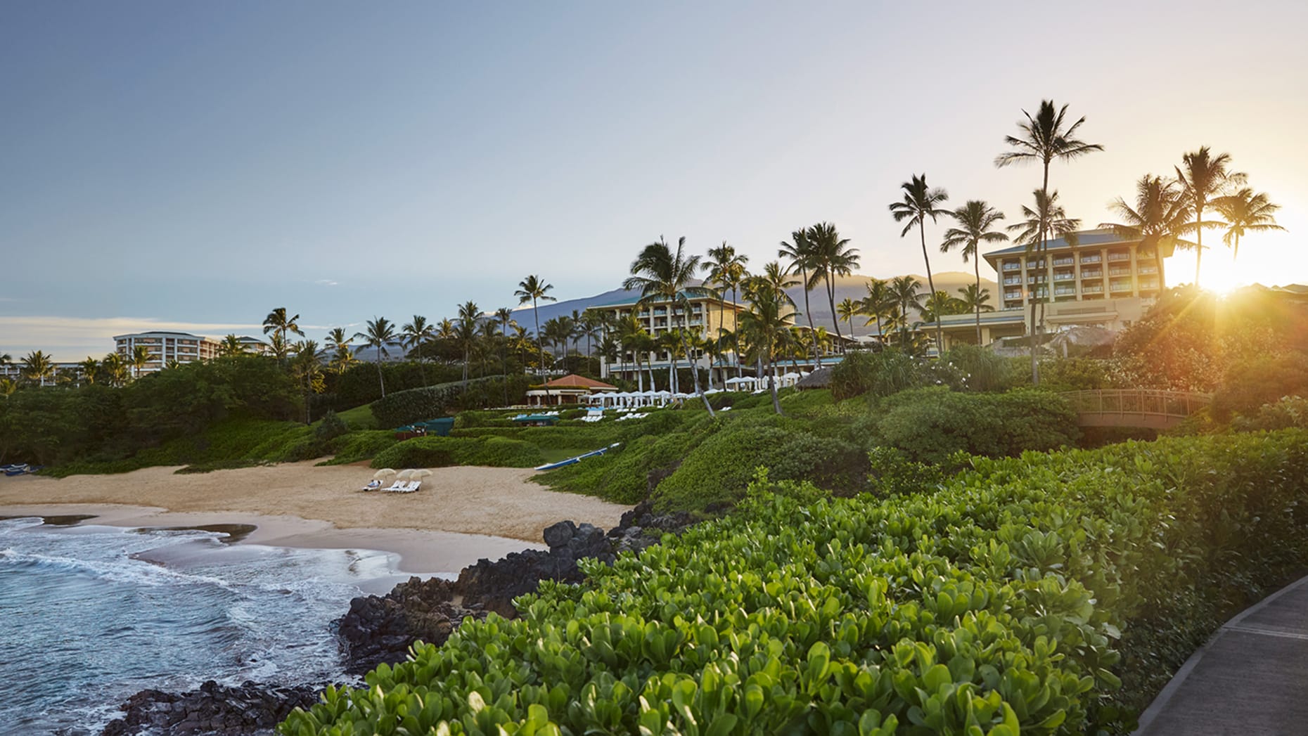 Palm-lined resort above a small beach on the Hawaiian coast at sunset