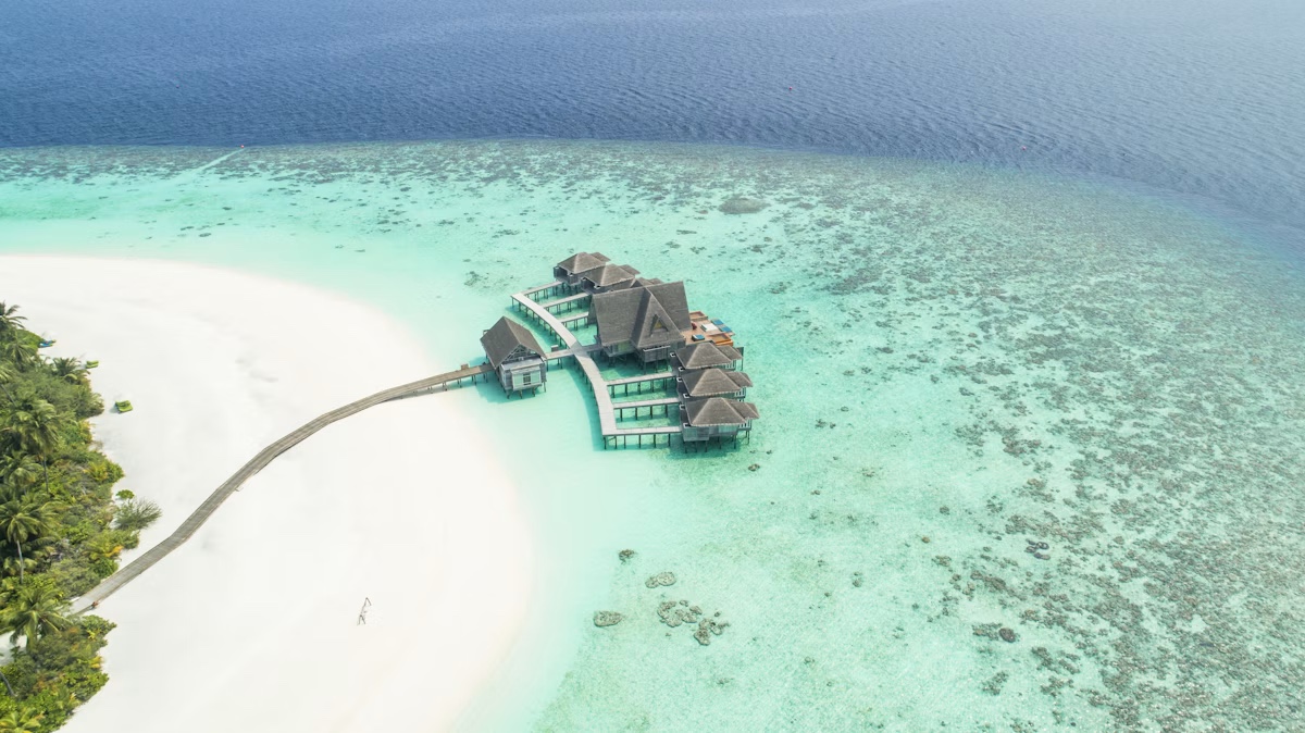 Aerial view of overwater villas beside a white sandbank