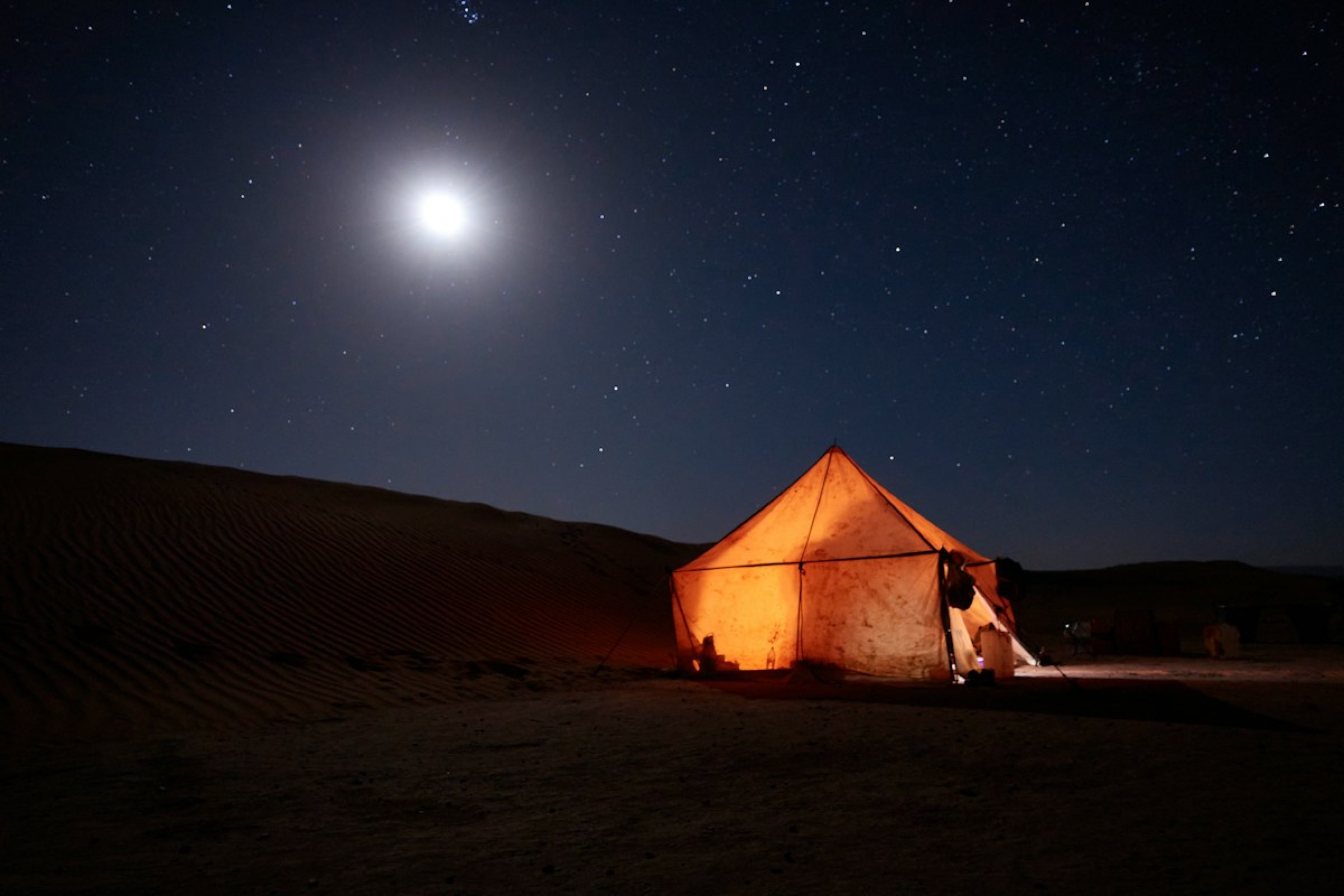 A lantern-lit desert tent under a starry sky