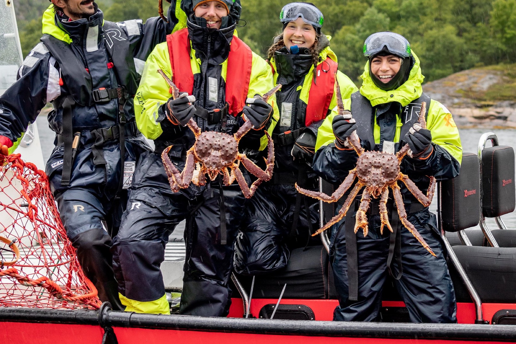 Travellers in survival suits holding king crabs on a boat in Kirkenes